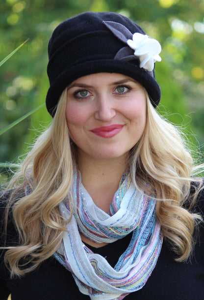 woman wearing black fleece cloche hat, with short brim, silver leaves and ivory flower. 