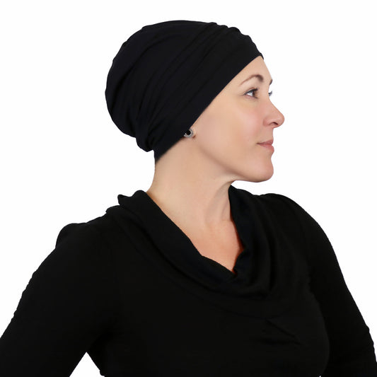 Woman wearing black slouchy beanie for chemo headwear. side view showing fullness in the back   